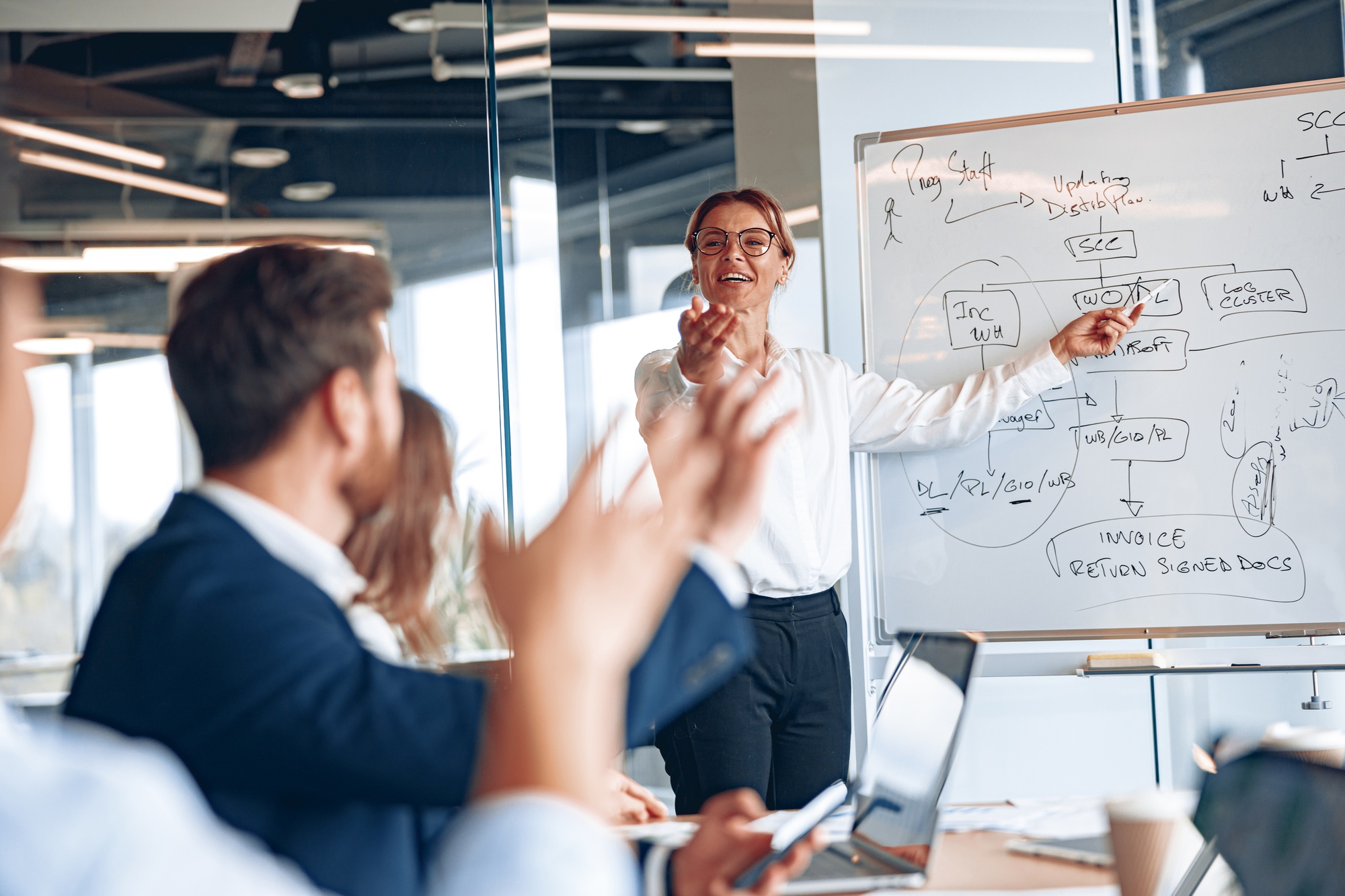 Experienced businesswoman by whiteboard explaining situation on the market to young managers