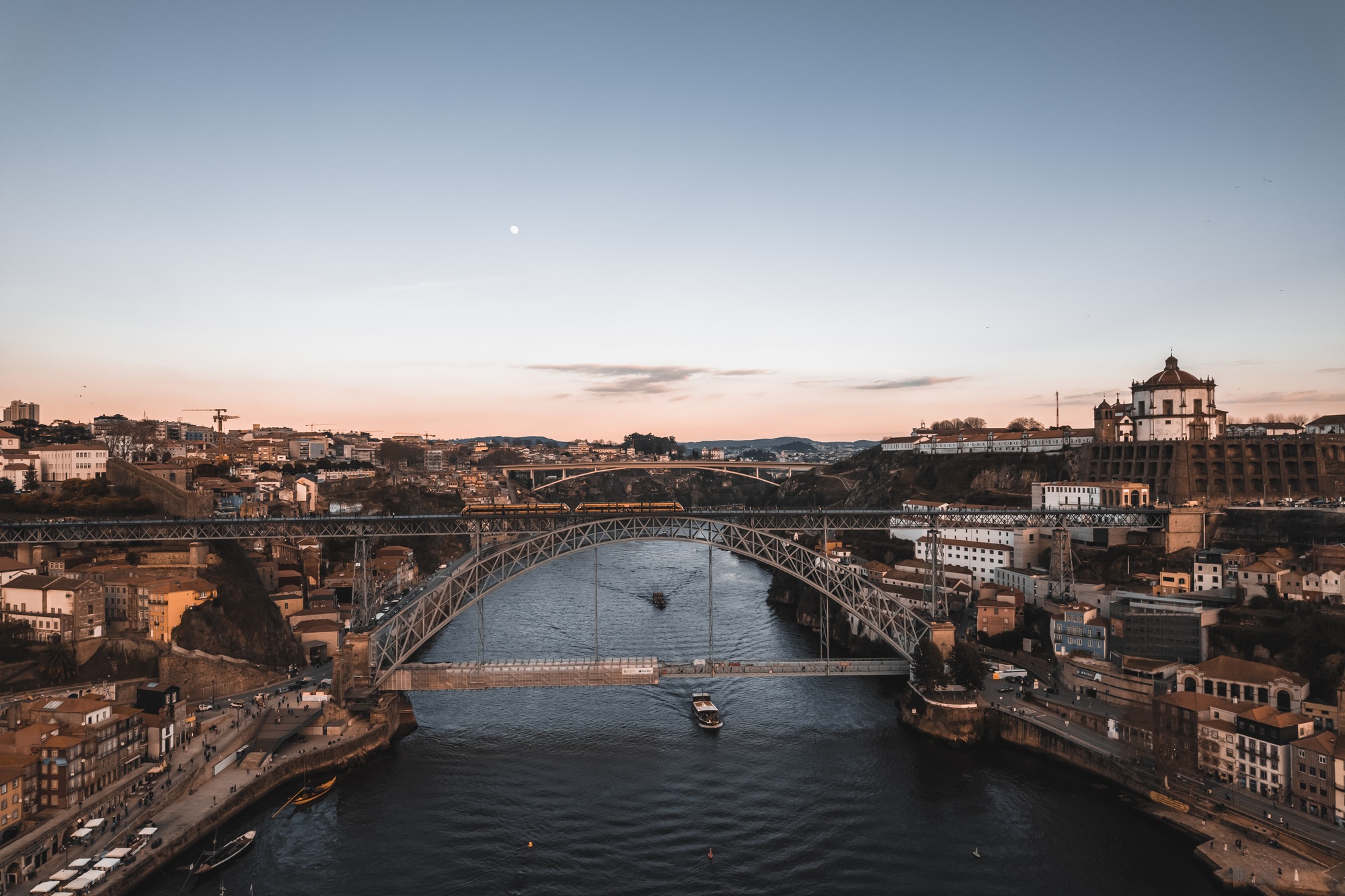 The train crosses the bridge in Porto. Sailing boats on the river in Porto.